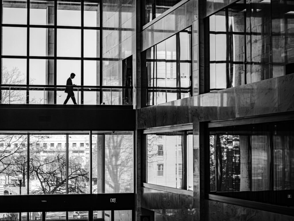 Person walking along a glass-walled office building walkway