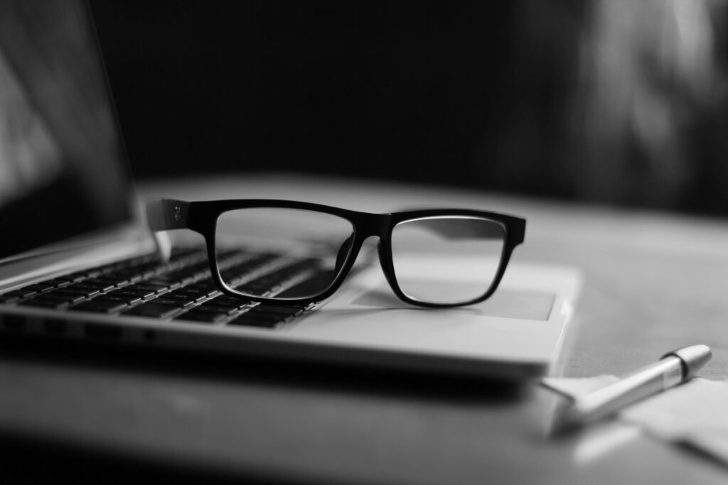 Glasses resting on a laptop keyboard beside a pen