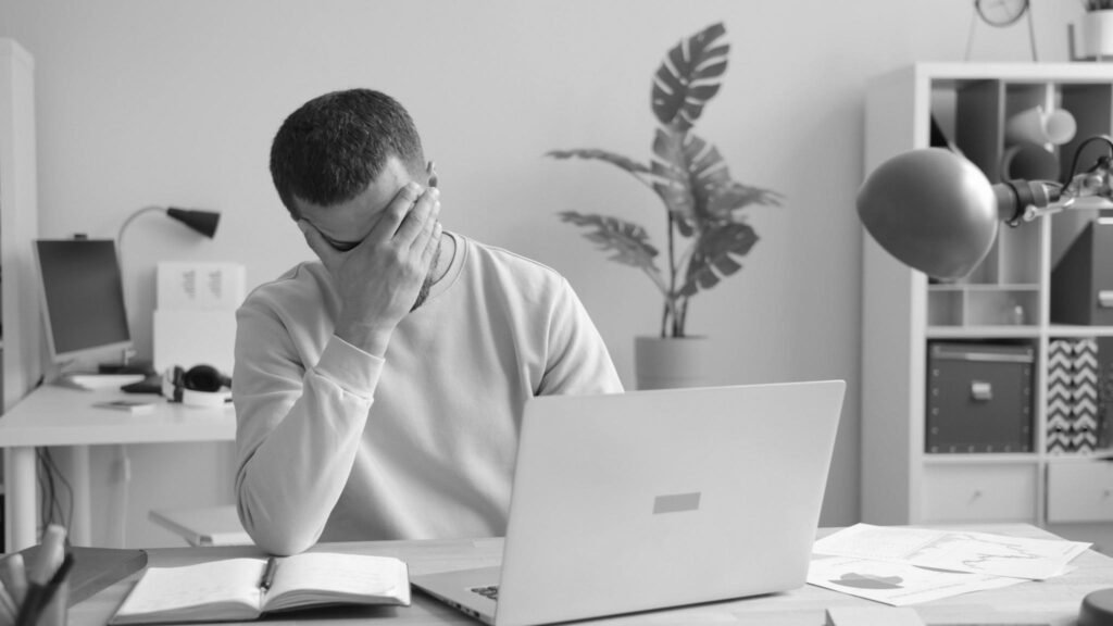 Professional at a desk with a laptop, head in hand
